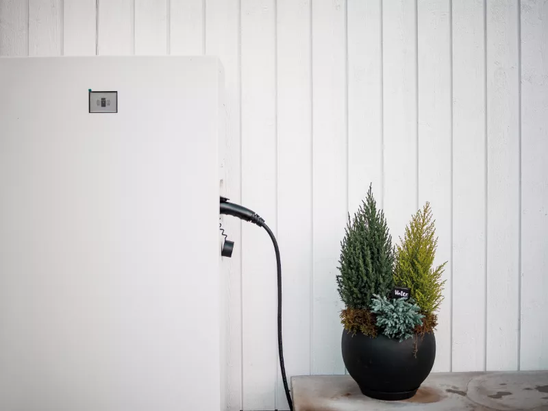 Batterilagring 1 Närbild på Emaldo hembatteri i Solna – anslutet och installerat intill yttervägg med dekorativa växter.
