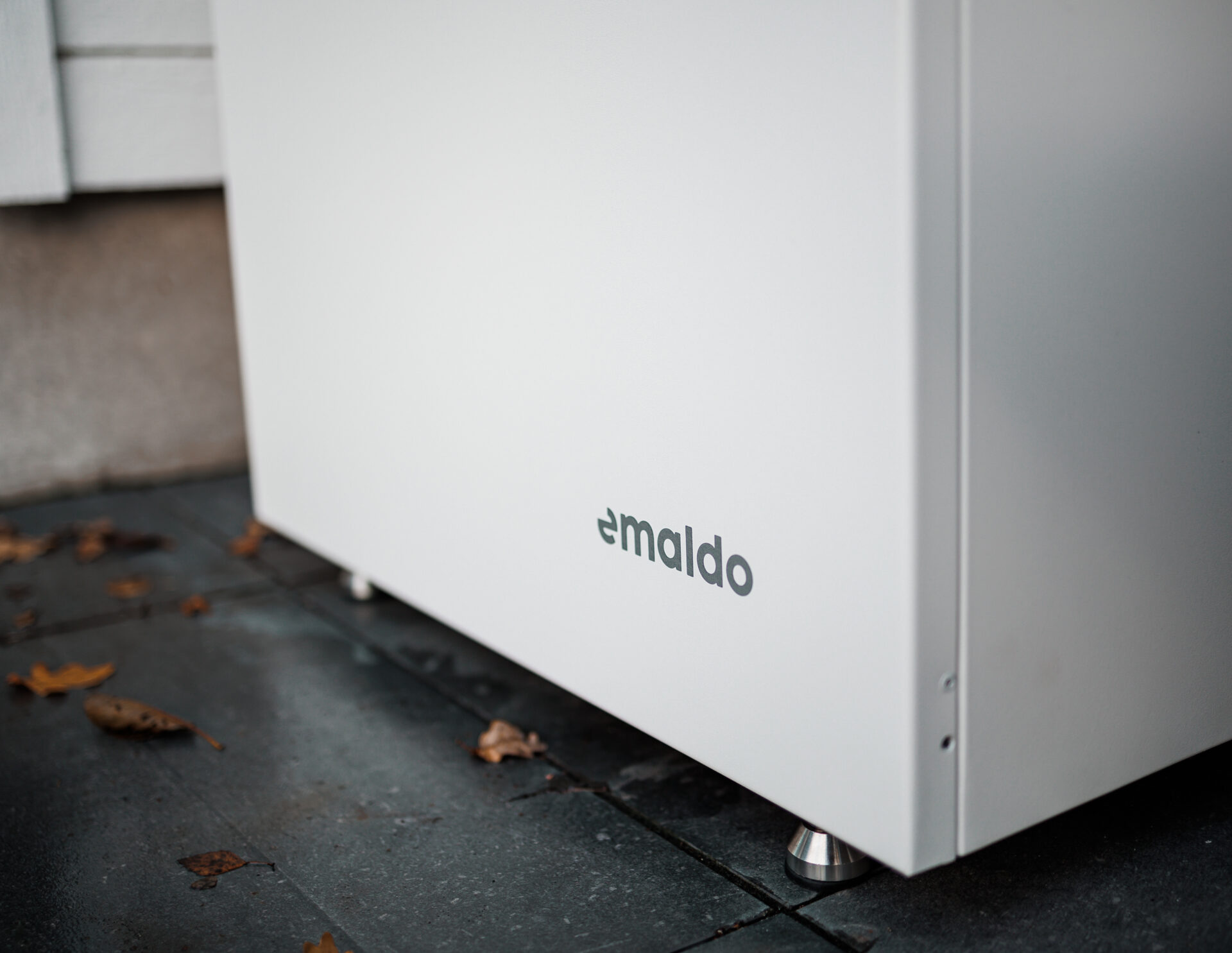 Batterilagring 24 Närbild på Emaldo-batterilagring på hembatteri installerat i Solna – omgiven av höstlöv på stensatt uteplats.